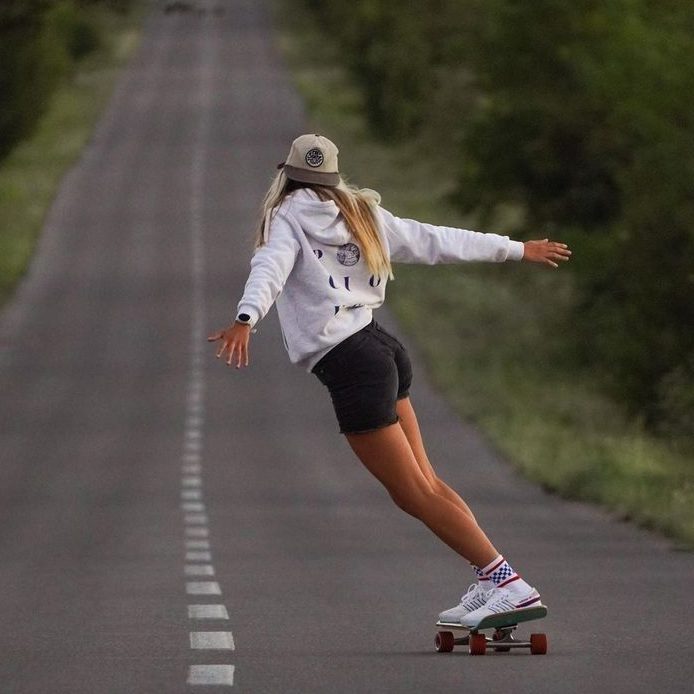 A woman skateboards down a road, showcasing her balance and skill in a dynamic outdoor setting.