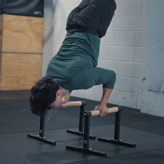 A man performing a handstand on a gym bar, showcasing strength and balance in a fitness environment.